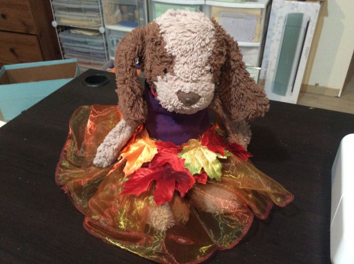 A well-worn stuffed bunny plush wears a tutu made of glimmering, iridescent tulle in bronze and green, decorated by silk leaves in red, gold, and green-tinged gold. (This is a handicraft and not an illustration.)